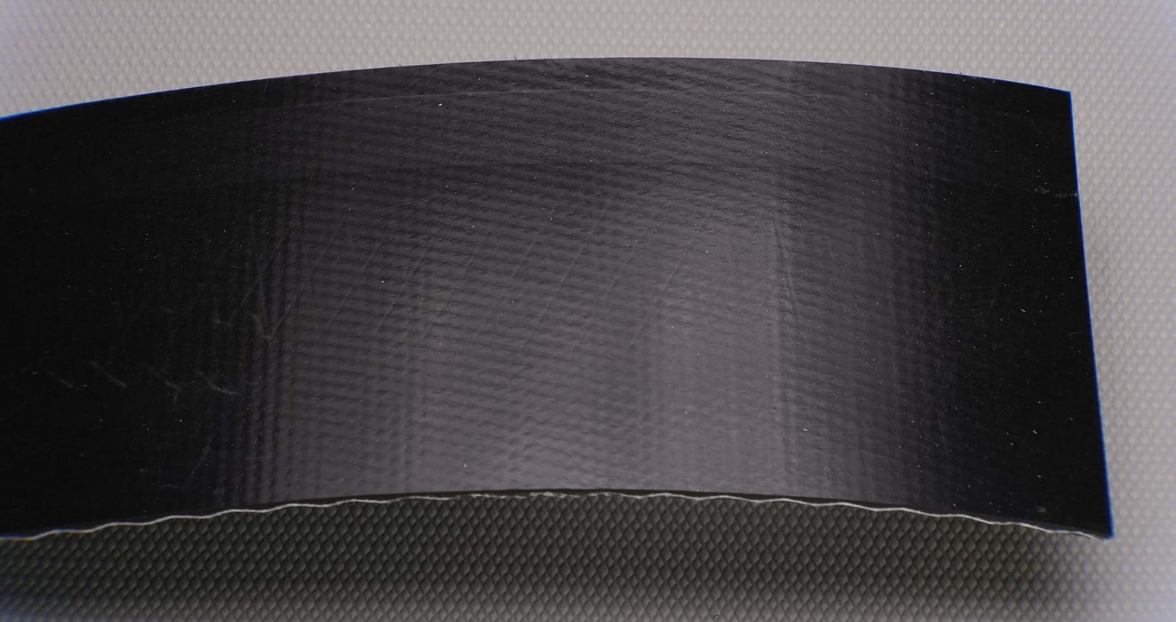 Front view of a PVC conveyor belt with a smooth top and brush bottom. The belt is 9/64" thick, with a black top and bottom, and a strength of 1% elongation at 0.073 lbs/in.