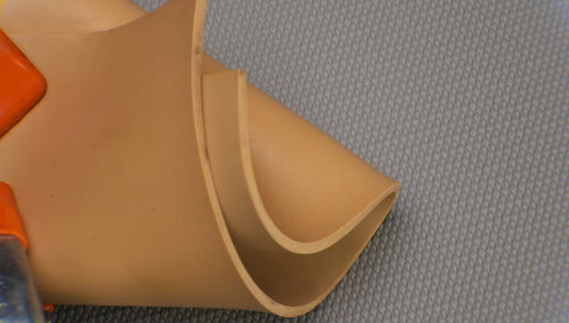 Second photo showing flexibility and materials of both sides of Puregum tan rubber with 1/8 inch thickness, tan color, 40 durometer, 3000 psi tensile strength, and 700% elongation.