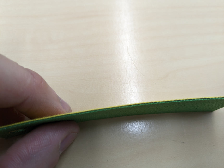 Side view of NC nylon conveyor belt on a sample showing 0.8 nm thickness, yellow top and green bottom, fabric material, 1 layer, 1% elongation at 1.8 N/mm.
